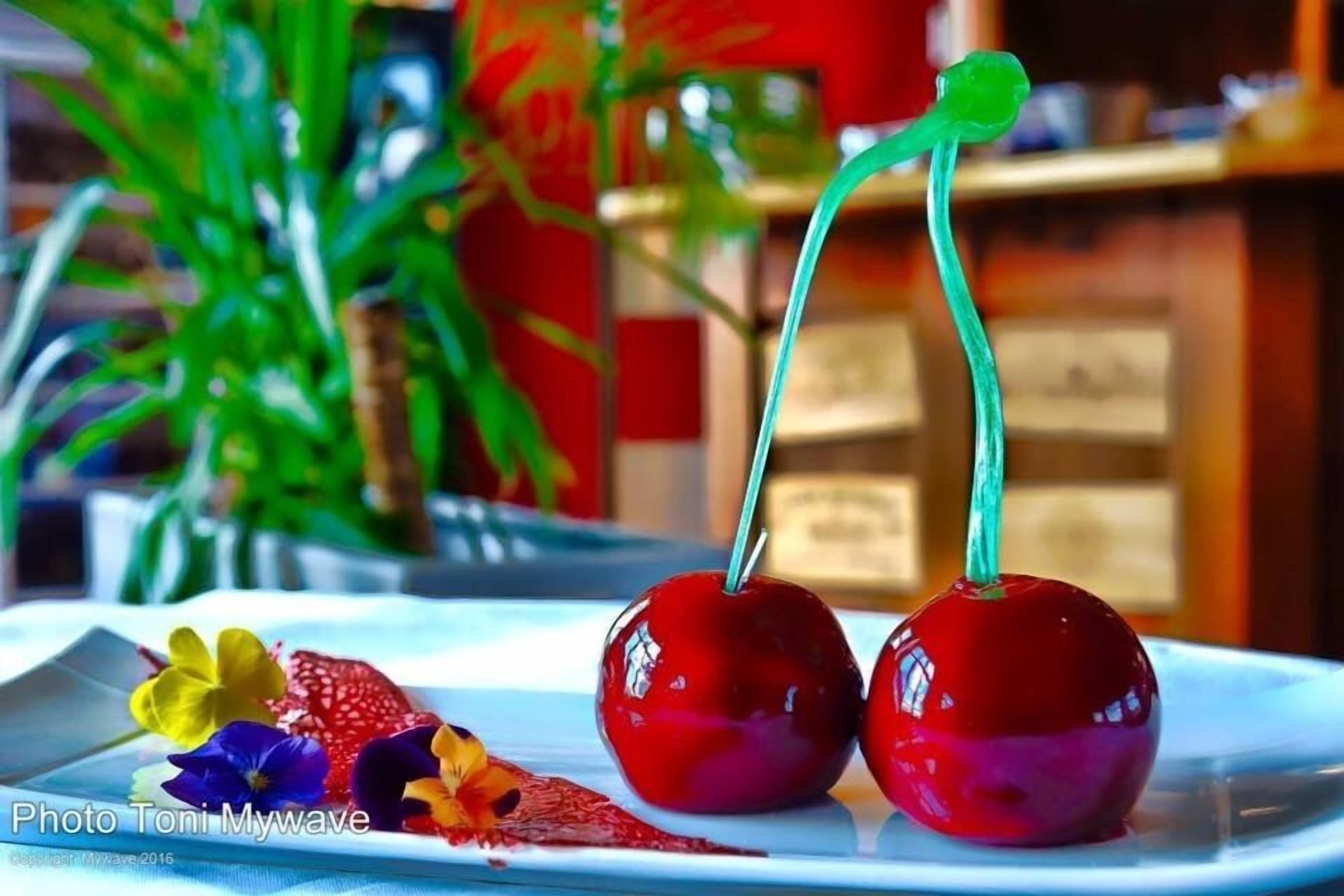 Dos manzanas rojas con tallos verdes sobre un plato blanco, acompañadas de flores coloridas.