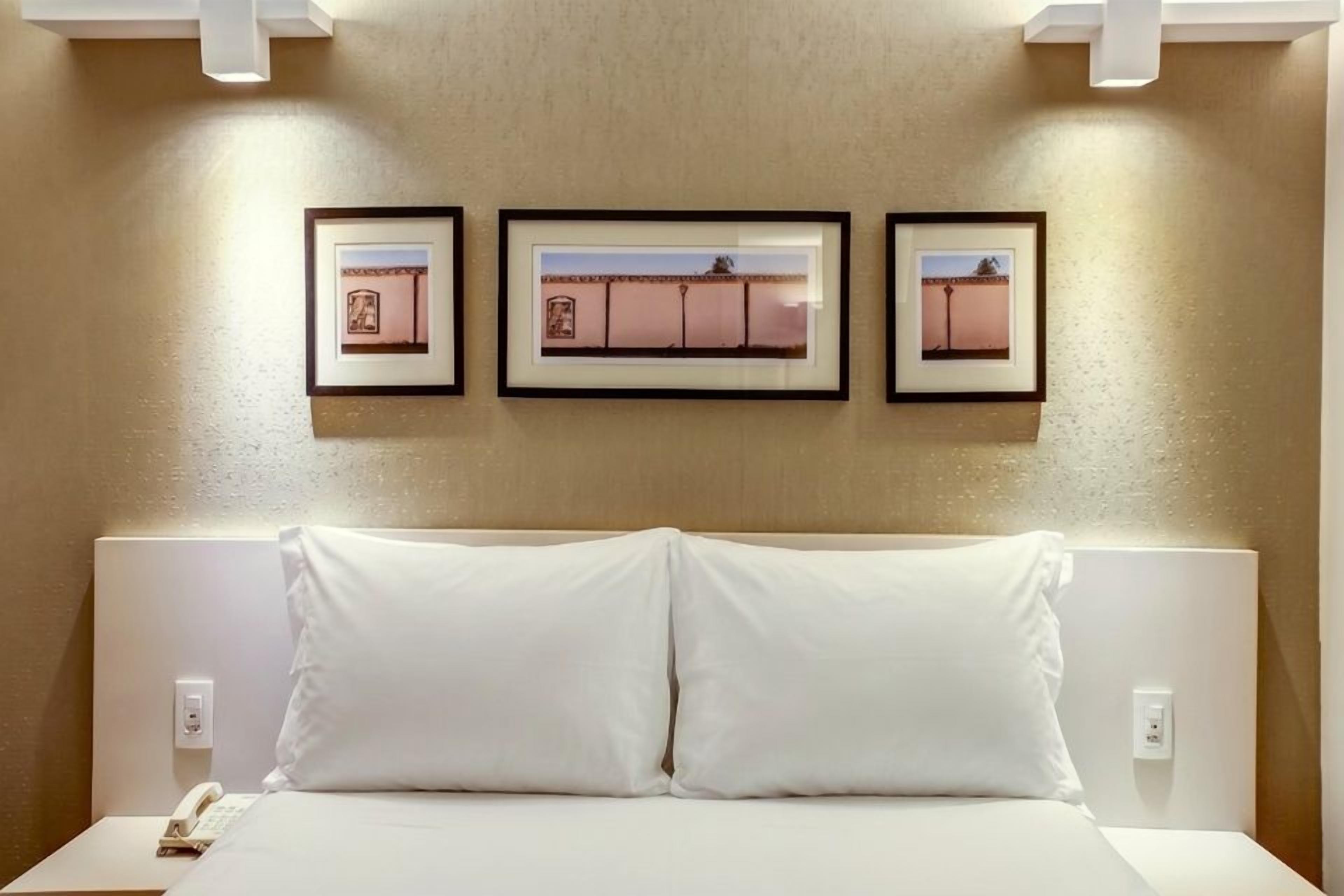 A hotel room with a bed, a nightstand, and three framed pictures on the wall.