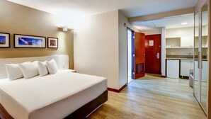 Habitación de hotel con una cama grande, piso de madera, kitchenette y una puerta que da a un baño.