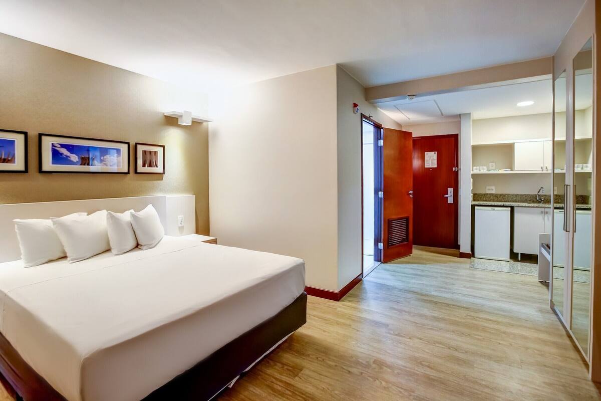 Een hotelkamer met een groot bed, een houten vloer, een kitchenette en een deur naar een badkamer.