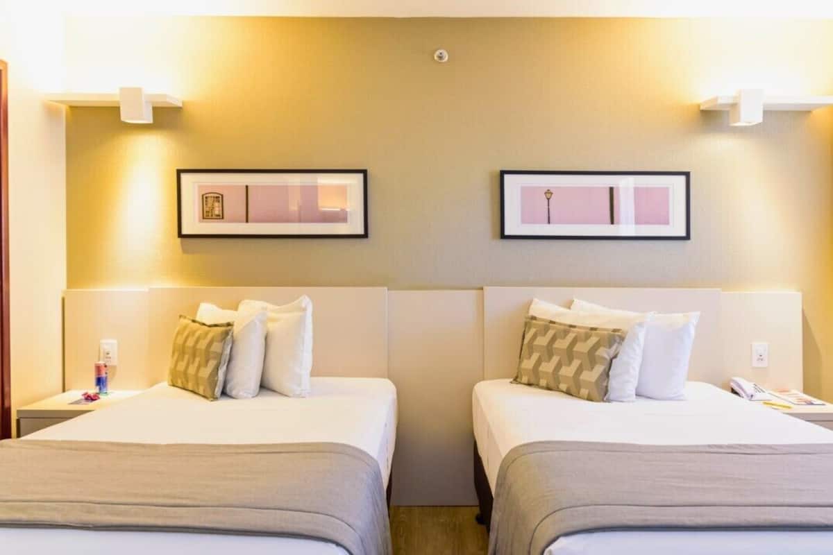 Een hotelkamer met twee bedden, elk voorzien van een hoofdeinde, nachtkastje en een ingelijst schilderij erboven.