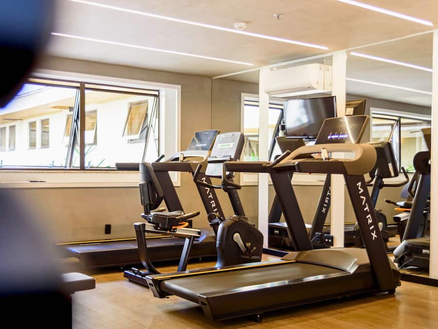 Uma academia com várias esteiras e equipamentos de ginástica, janelas amplas e design de interiores moderno.