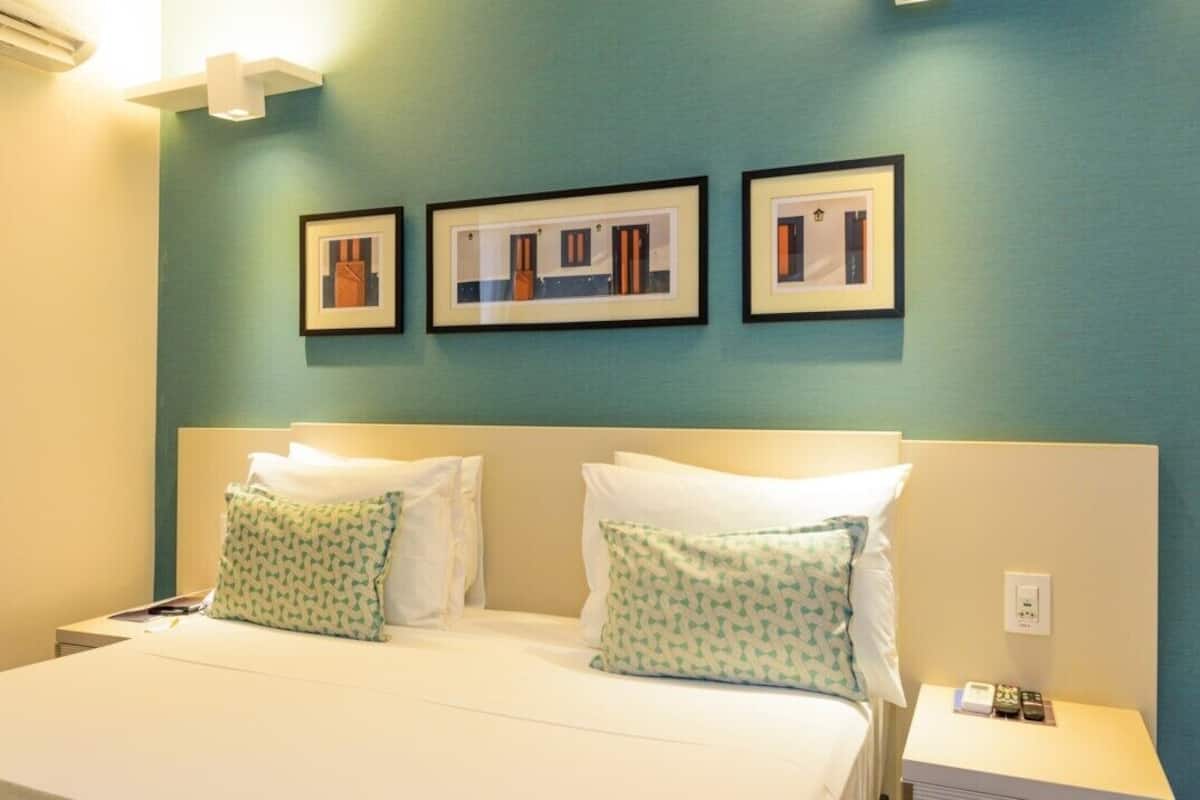 Een hotelkamer met een bed, twee kussens, een nachtkastje en drie ingelijste foto's aan de muur.