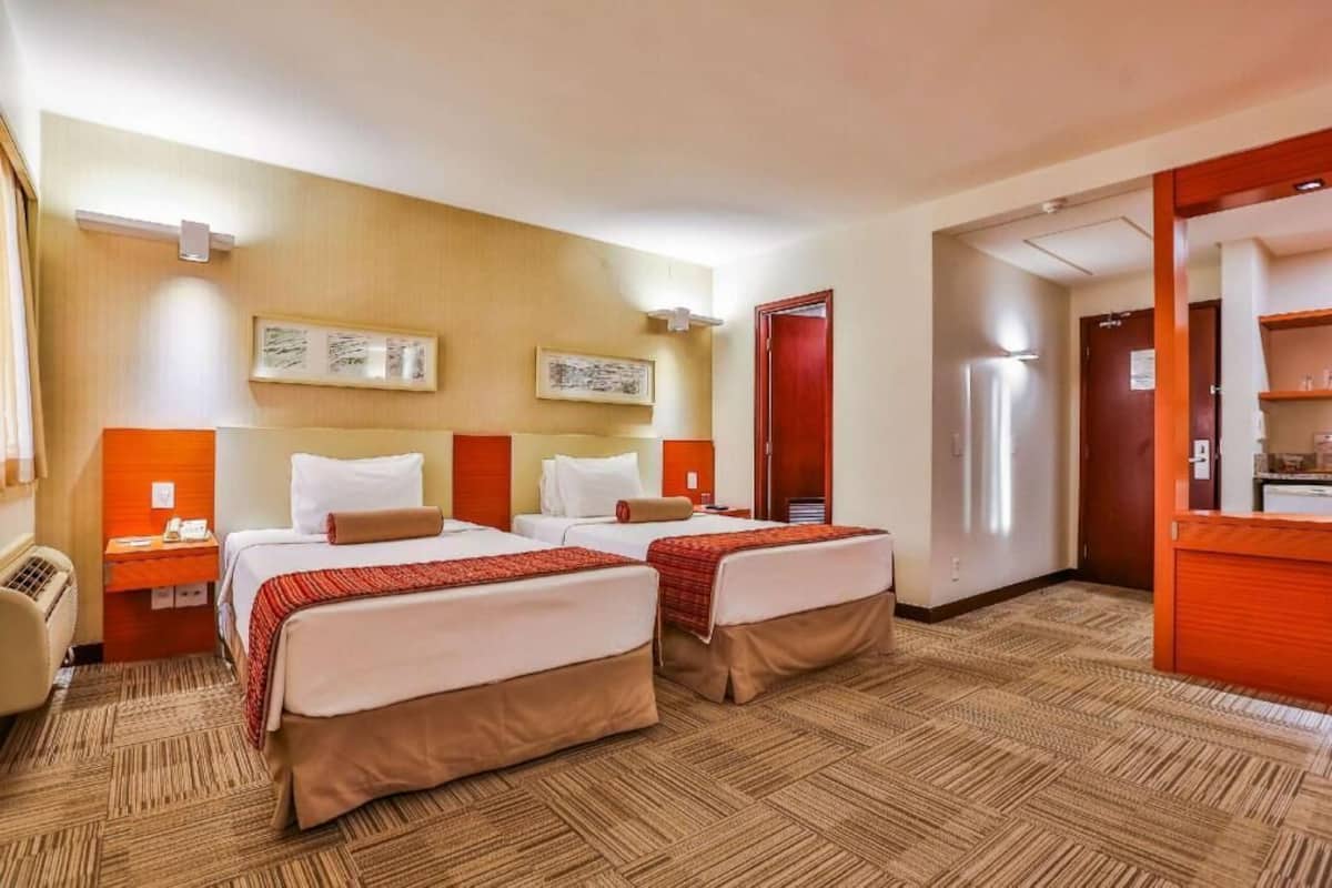 Een hotelkamer met twee bedden, een bureau, een stoel, een koelkast en een houten deur.