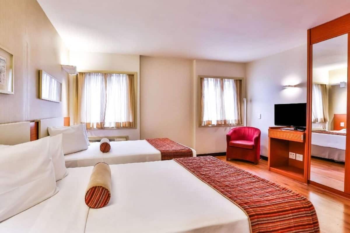 Een hotelkamer met twee bedden, een rode stoel, een televisie en een spiegel.