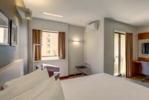 Una habitación de hotel con cama, sillón, televisión y ventana con cortinas.