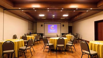 Un salón de conferencias con varias mesas y sillas, una pantalla de proyector mostrando una presentación y un techo de madera.