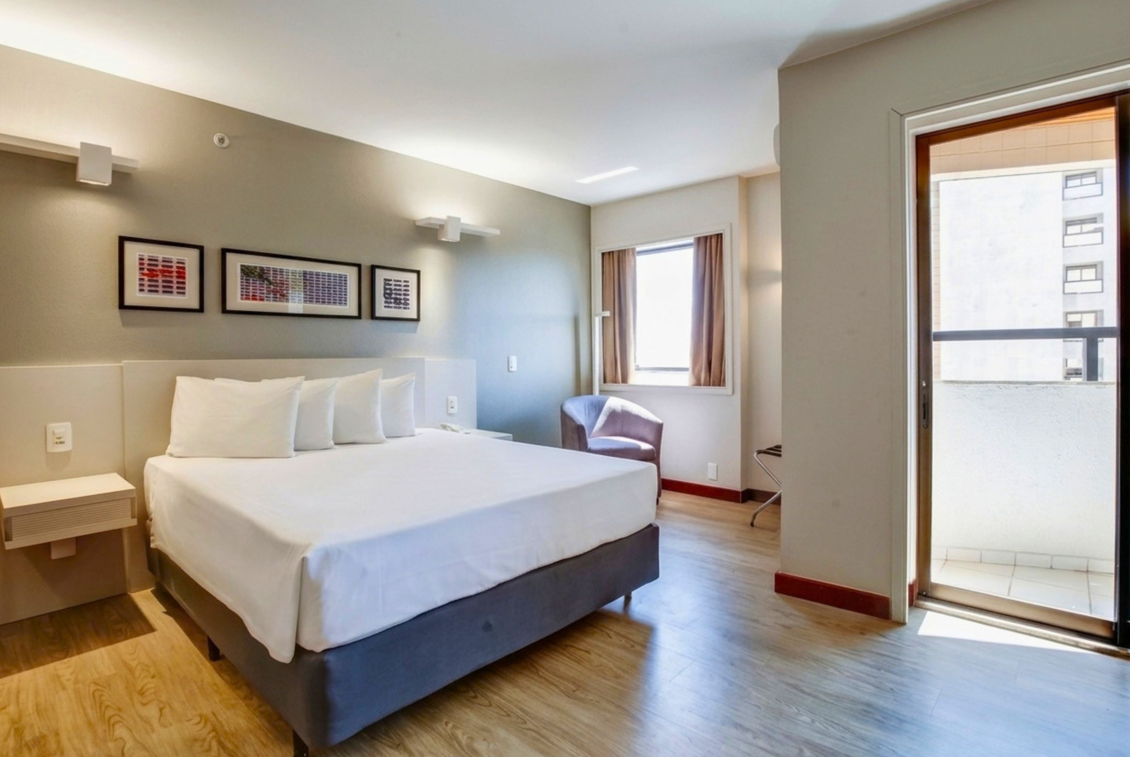 A modern hotel room with a large bed, a desk, a chair, and a balcony.