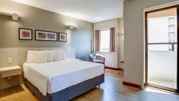 A modern hotel room with a large bed, a desk, a chair, and a balcony.