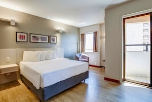 Habitación de hotel moderna con una cama grande, un escritorio, una silla y un balcón.