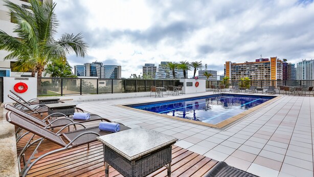 Un área de piscina en la azotea con sillones de descanso, una mesa y vistas al horizonte de la ciudad.