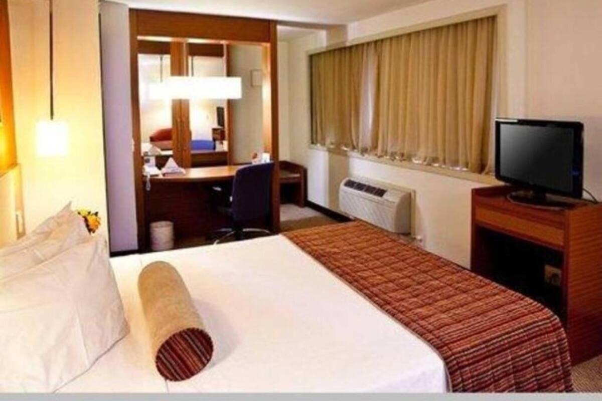 Een hotelkamer met een bed, een bureau, een stoel, een televisie en een raam met gordijnen.