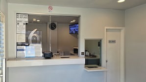 A hotel reception area with a no smoking sign, a clock, and a checkout counter. - Motel 6 Los Angeles, CA - Downtown (Los Angeles)