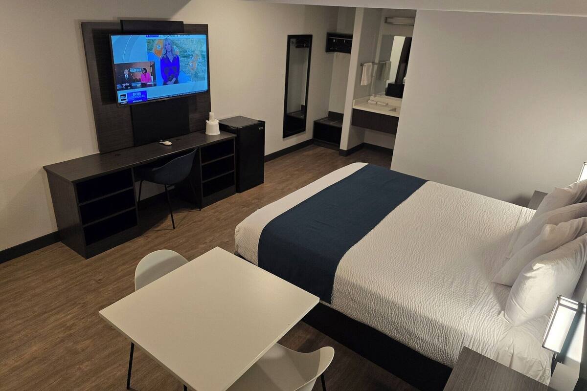 Ein Hotelzimmer mit Bett, Schreibtisch, Stuhl, Fernseher und Spiegel.