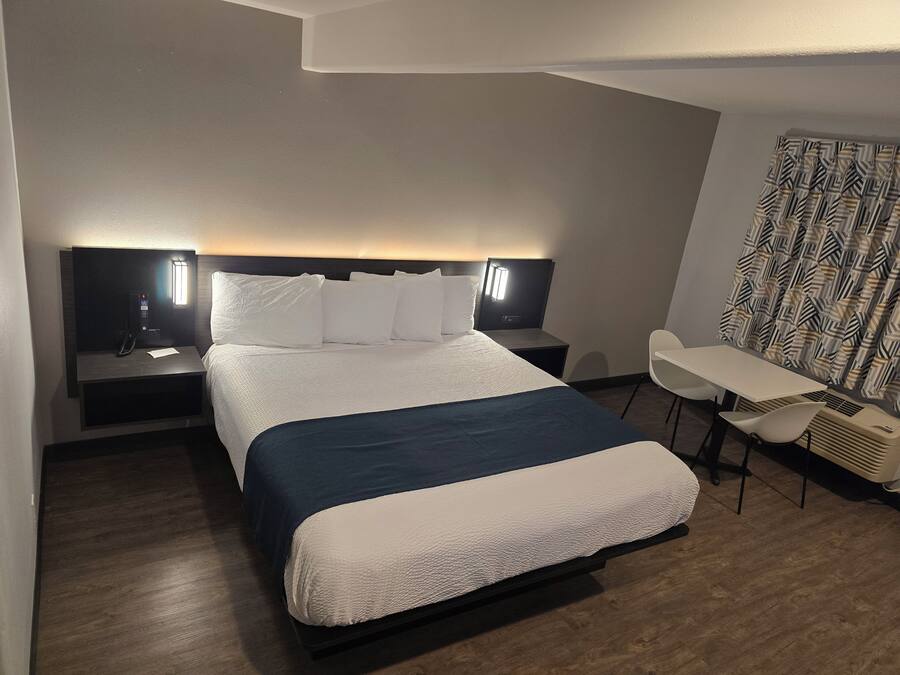 A hotel room with a bed, bedside tables, a desk, and a chair.