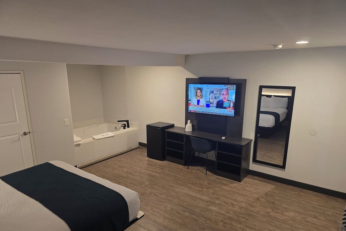 Ein Hotelzimmer mit Bett, Schreibtisch, Fernseher, Spiegel und Badewanne.