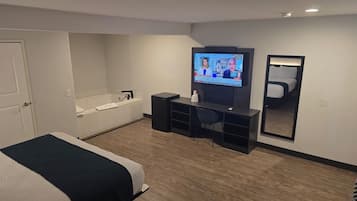 A hotel room with a bed, a desk, a TV, a mirror, and a bathtub.
