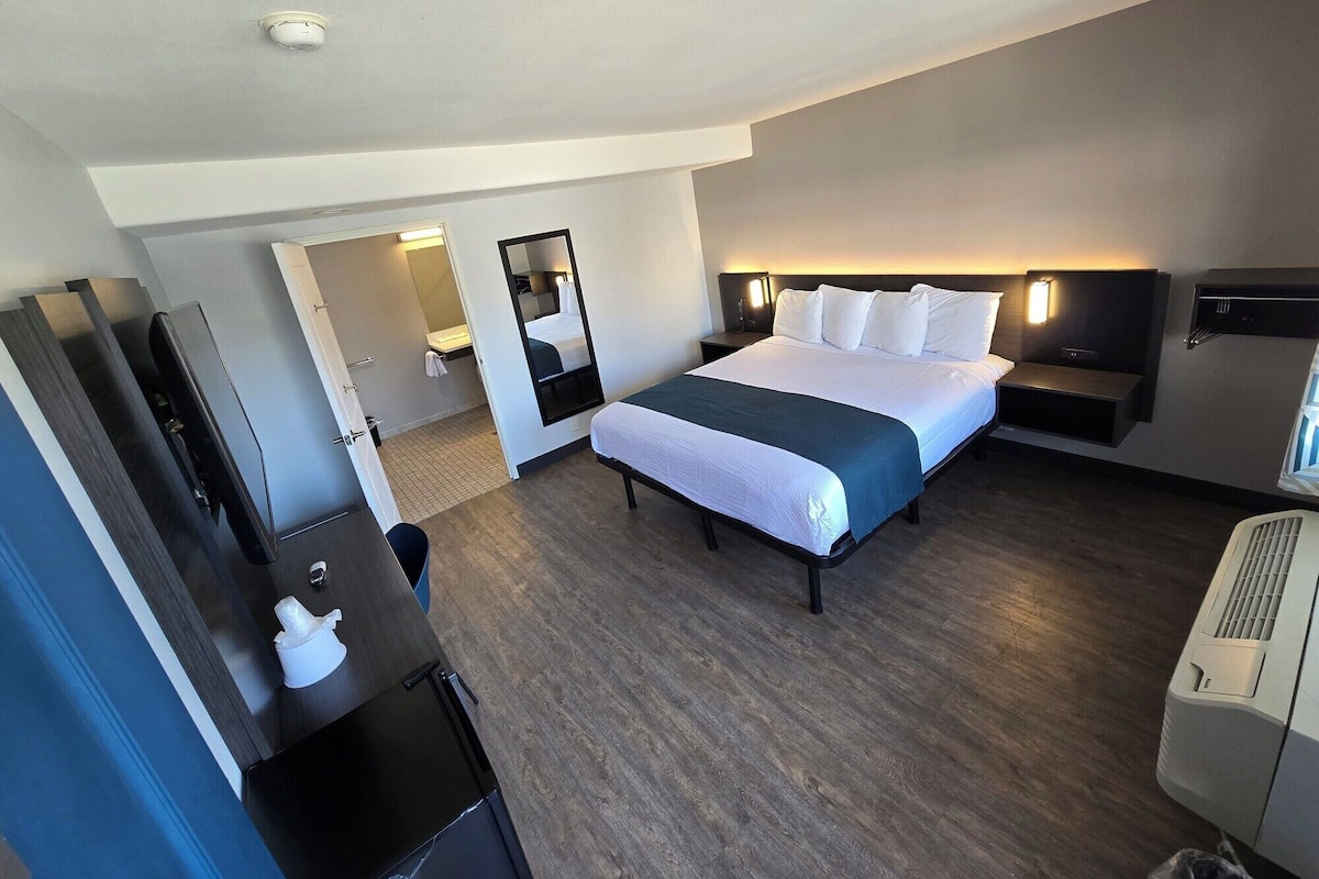 Ein Hotelzimmer mit einem großen Bett, einem Schreibtisch mit Stuhl, einem Spiegel und einem Wandheizkörper.