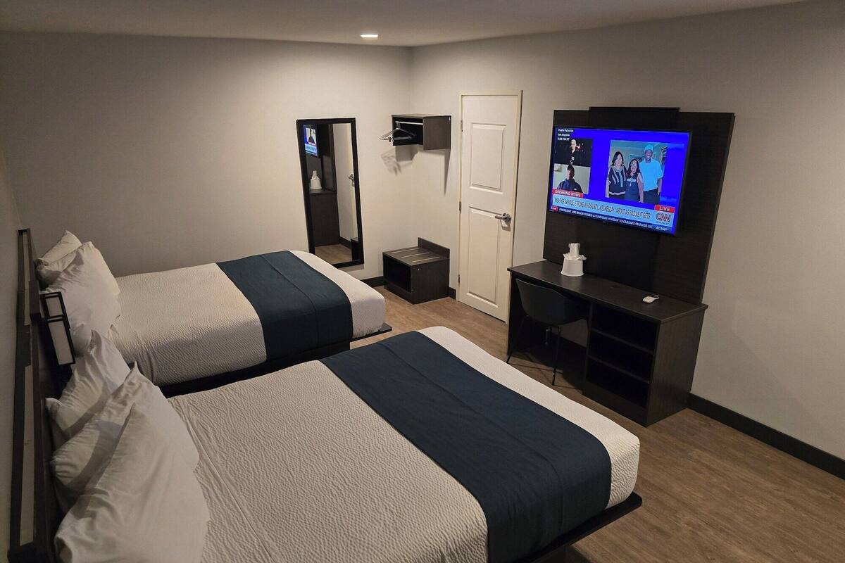 Ein Hotelzimmer mit zwei Betten, einem Fernseher, einem Schreibtisch und einer Tür.