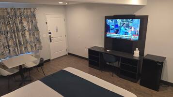 Een hotelkamer met een bed, een bureau, een stoel, een televisie en een klein kastje.