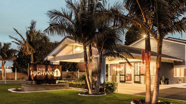 Un hotel con un letrero que dice "Inn at Highway 1", rodeado de palmeras y un césped bien cuidado.