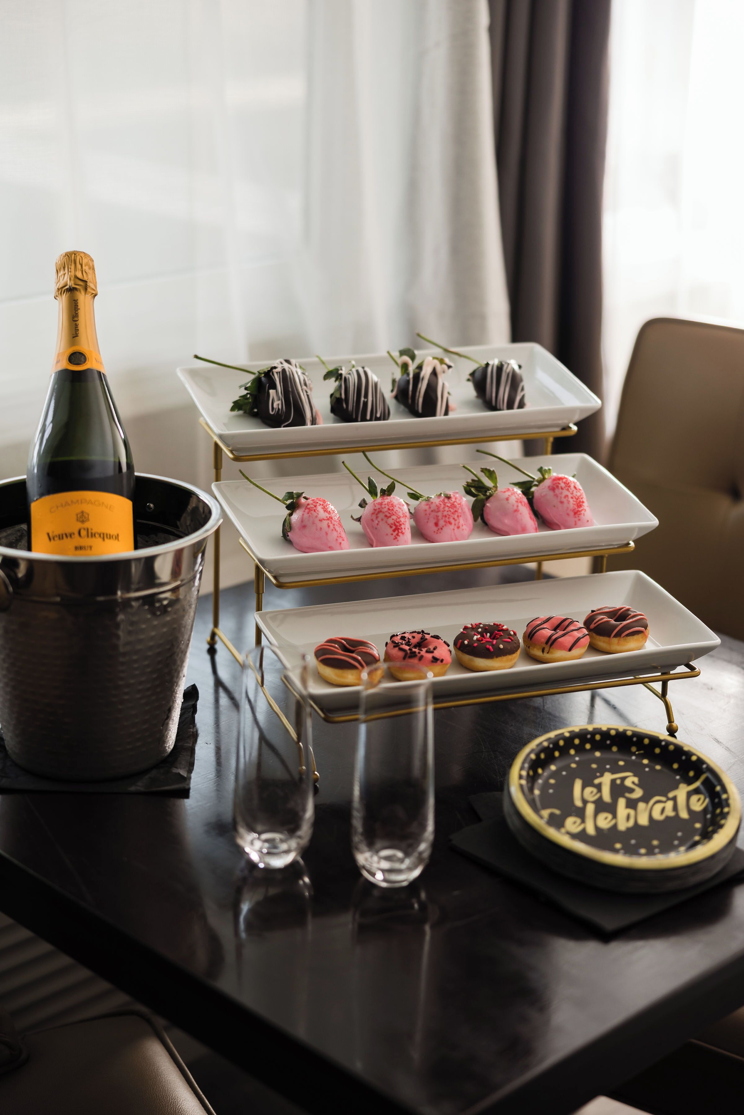 Ein Tisch mit einer Champagnerflasche, drei Desserttabletts und einer Torte, auf der 'Lasst uns feiern' steht.