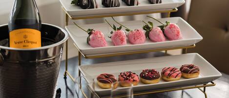 A table with a bottle of champagne, three dessert trays, and a cake with "let's celebrate" written on it.