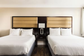 A hotel room with two beds, a nightstand, and a bedside table with a lamp.