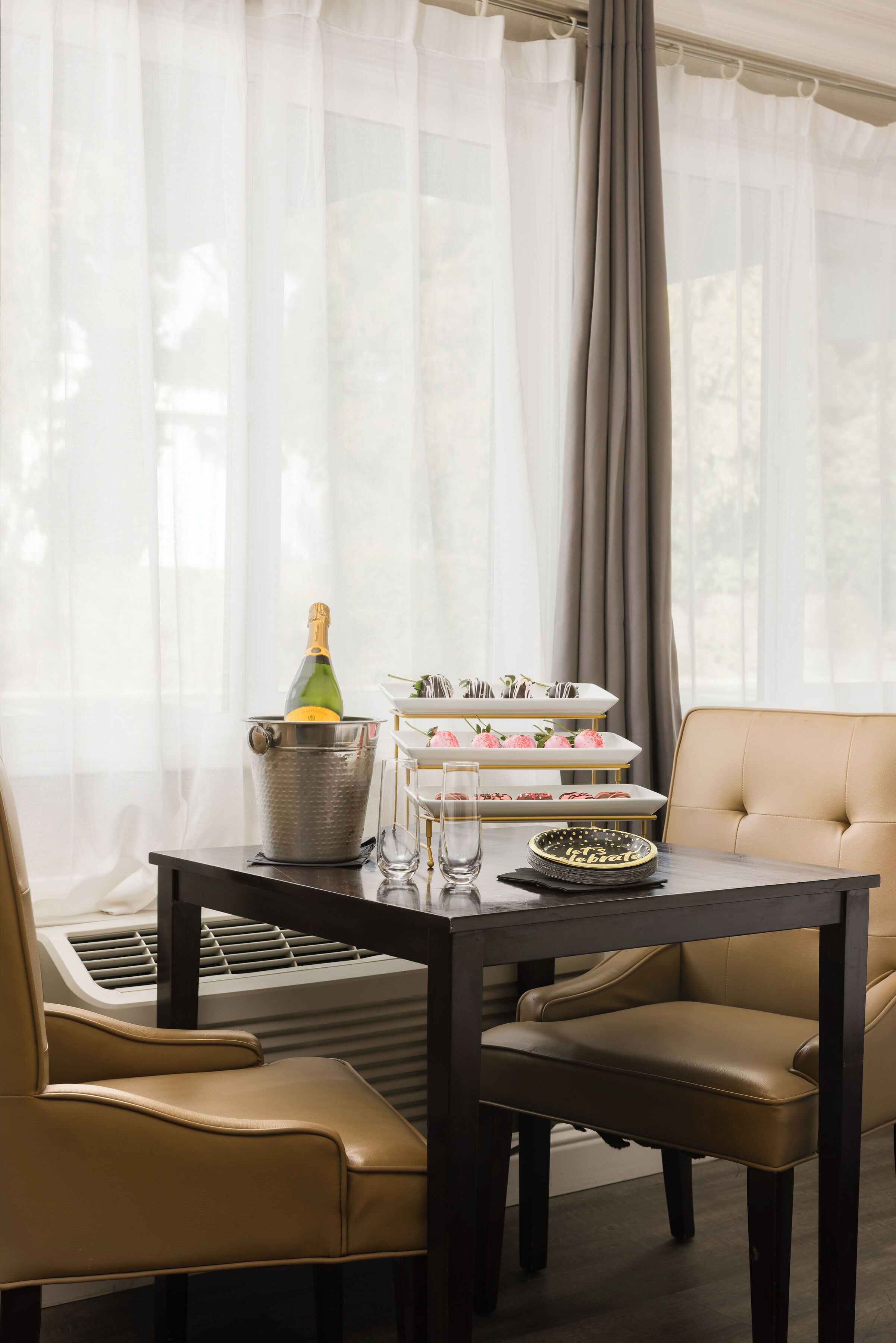 A dining area with a table set for two, a champagne bottle, and a dessert display.
