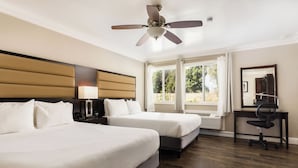 Habitación de hotel con dos camas, un escritorio con silla, un ventilador de techo y un ventanal con cortinas.