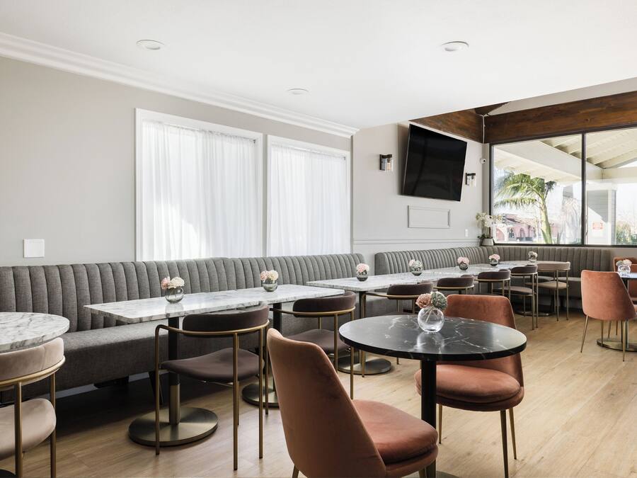Um restaurante moderno com mistura de mesas redondas e retangulares, assentos acolchoados e uma grande tela de televisão.