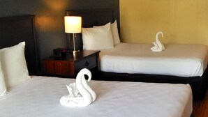 Two beds with white linens and swan-shaped towels, a bedside lamp, and a nightstand with a clock. - Econo Lodge Ormond Beach North - Daytona (Ormond Beach)