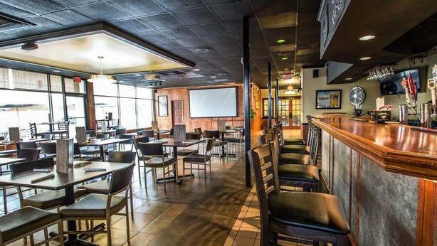 A restaurant with a bar area, tables, chairs, and a projection screen. - Econo Lodge Ormond Beach North - Daytona (Ormond Beach)