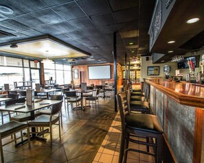 Un ristorante con area bar, tavoli, sedie e uno schermo di proiezione.