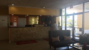 A reception area with a receptionist, a reception desk, a sofa, and a large window. - Econo Lodge Ormond Beach North - Daytona (Ormond Beach)