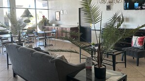 A modern living room with a grey sofa, a glass coffee table, and several potted plants. - Econo Lodge Ormond Beach North - Daytona (Ormond Beach)
