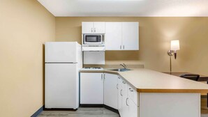 A compact kitchen with white cabinets, a microwave, a refrigerator, and a small island with a sink.