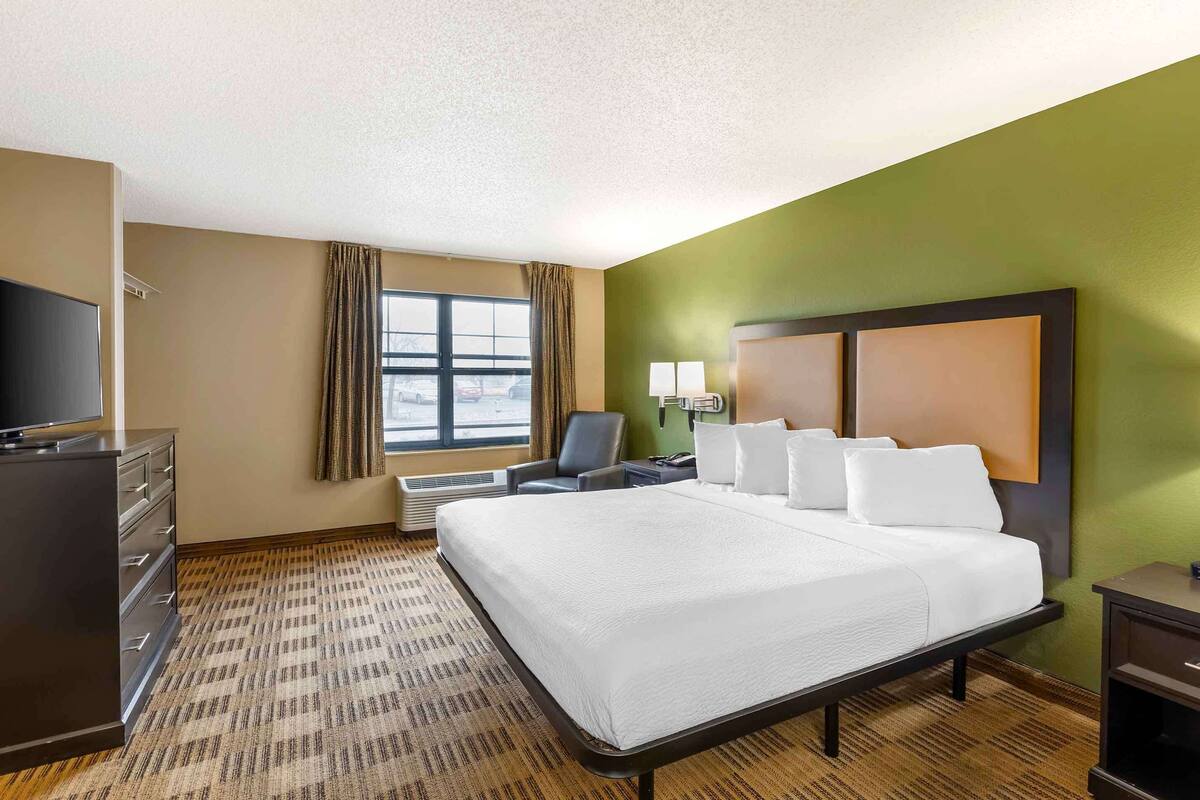 A hotel room with a large bed, a desk, a chair, a television, and a window with curtains.