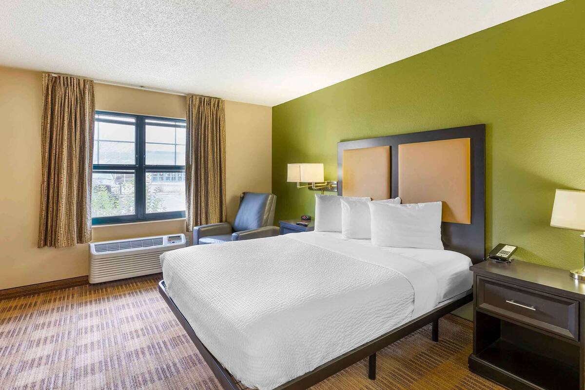 A hotel room with a large bed, a desk, a chair, and a window with curtains.