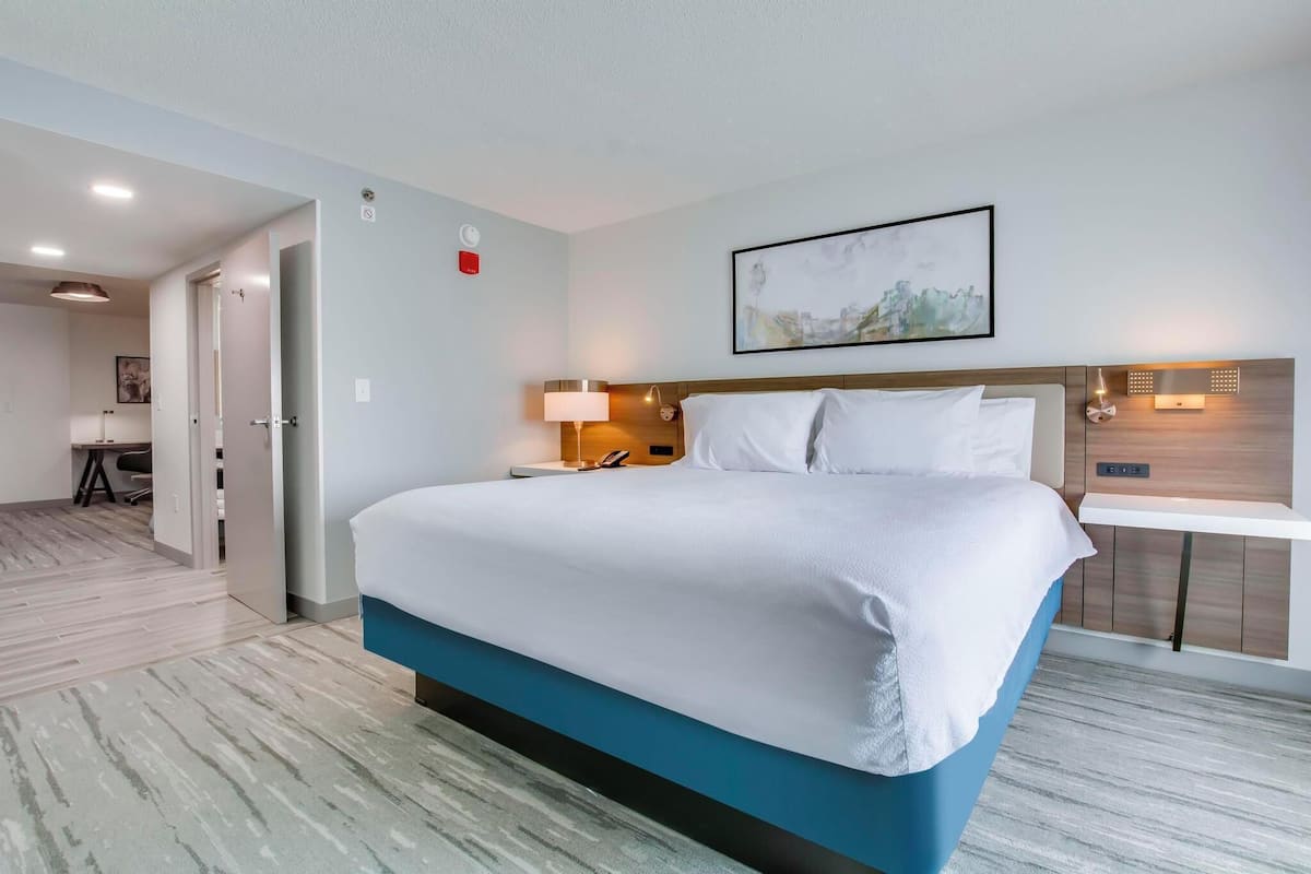 A modern hotel room with a large bed, bedside table, and a wall-mounted light.