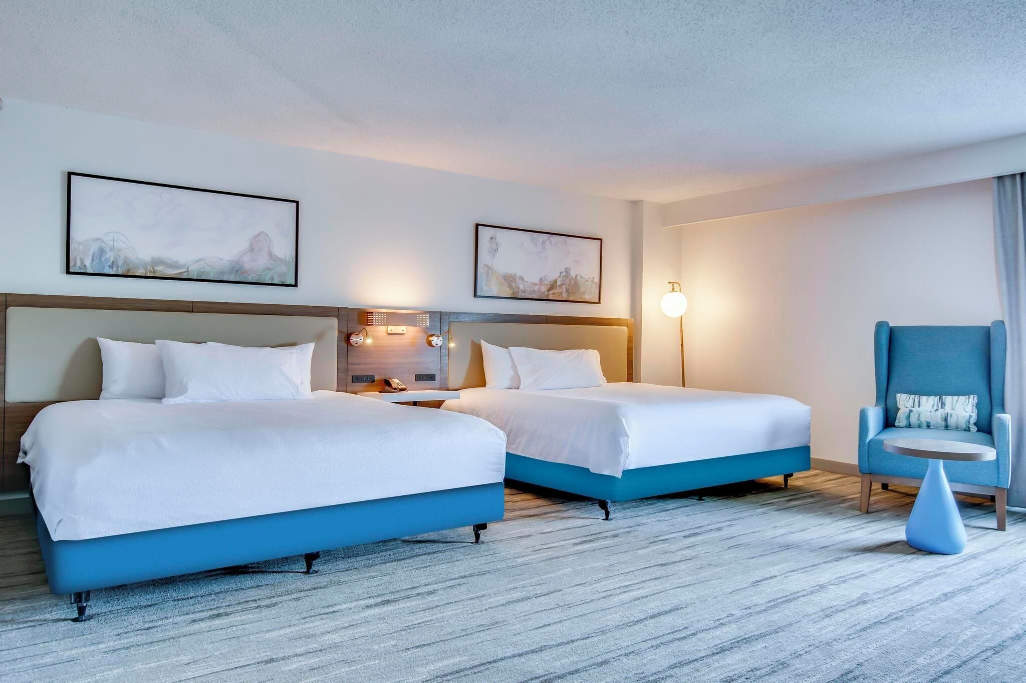 A hotel room with two beds, a desk, a chair, and artwork on the walls.