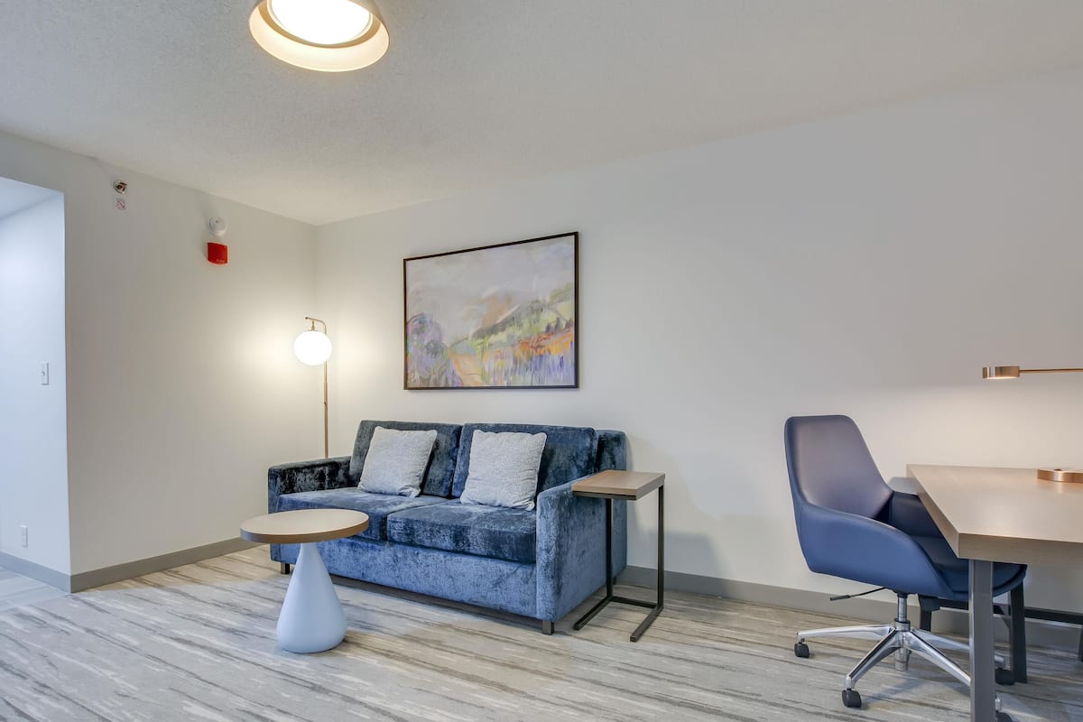 A modern room with a blue sofa, a small round table, a desk, and a chair.