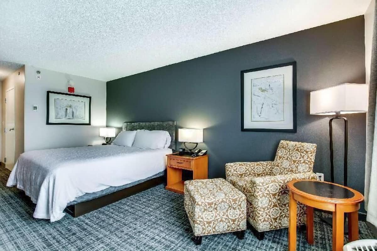 A hotel room with a bed, two chairs, a small table, a nightstand, and two wall-mounted lamps.