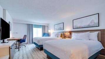 A hotel room with two beds, a desk, a chair, and a TV.