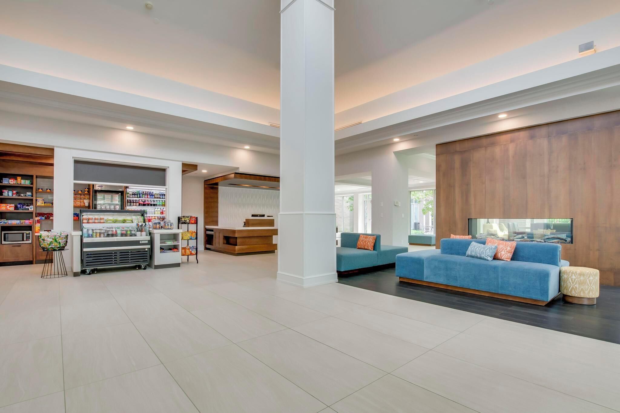 A spacious lobby with a blue sofa, a refrigerator with beverages, and a wooden reception desk.