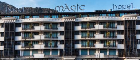 Un hotel amb balcons, un rètol que diu "MAGIC HOTEL" i diverses botigues a la planta baixa.