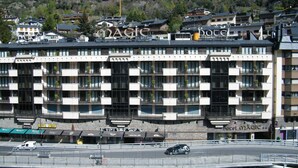A hotel with a modern architectural design, featuring balconies with plants, a prominent sign, and a view of the surrounding mountainous landscape.