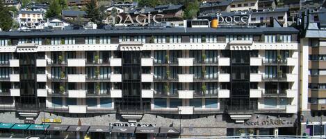 A hotel with a modern architectural design, featuring balconies with plants, a prominent sign, and a view of the surrounding mountainous landscape.