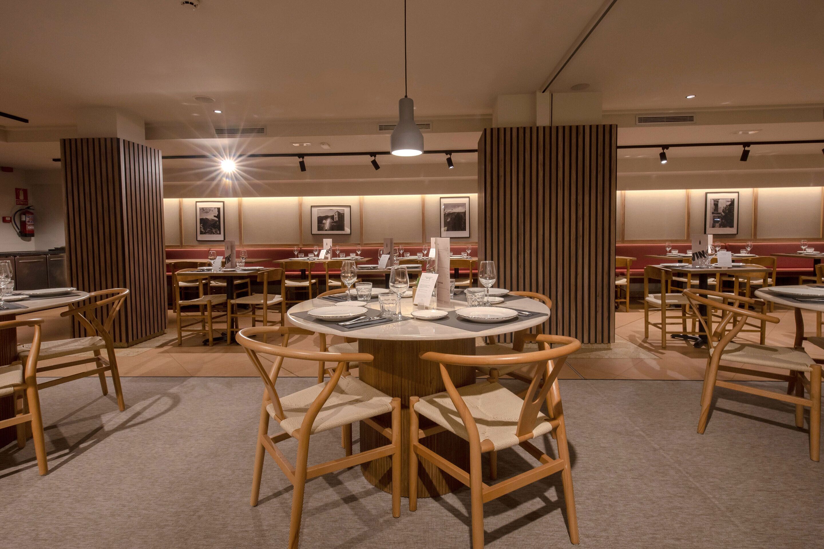 A restaurant with round tables and wooden chairs, equipped with menus and wine glasses.