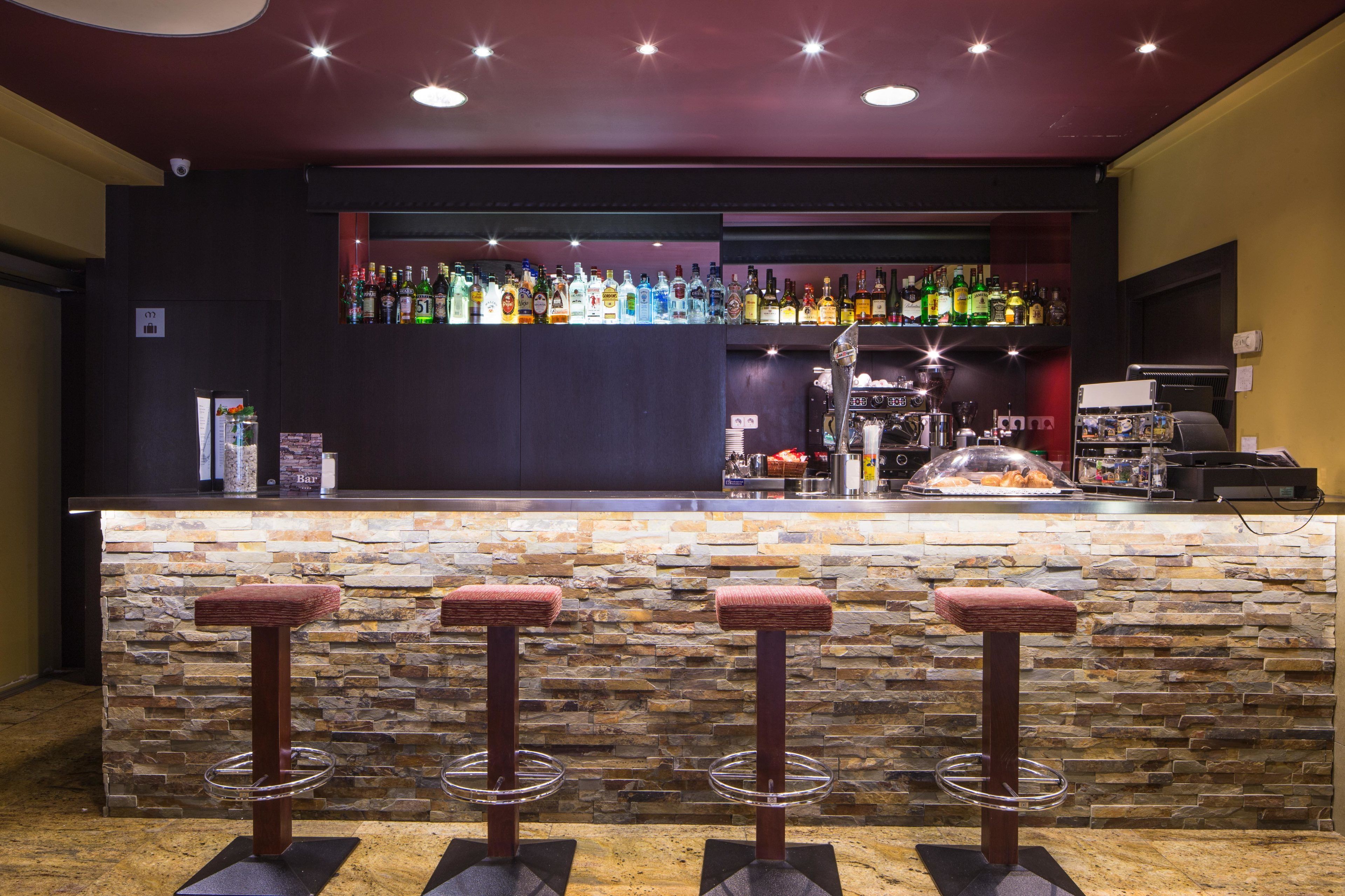 A bar area with a stone counter, multiple stools, and a variety of bottles.